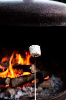 Person roasting over fire flames a marshmallows over campfire at night on a summer day, for smores or snack closeup