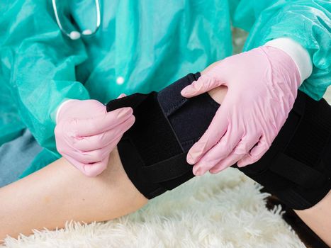 close-up of a family doctor putting a black brace on a patient's knee