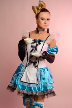 Young woman in erotic dress alice in wonderland holds a cup and saucer on a pink background.