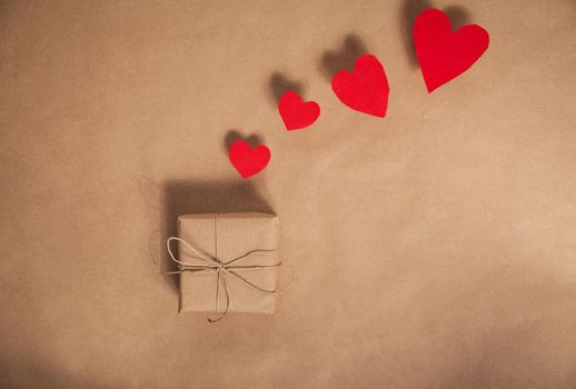 High angle view of a plain eco friendly brown paper wrapped for Valentines Day present with various red heart on brown paper background Copy space modern design.