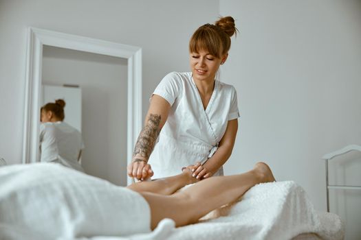Massagist woman is doing professional leg massage in modern salon