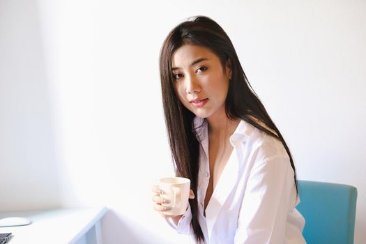 Smiling calm young woman drinking coffee at home