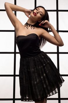 Attractive young brunette girl with red lipstick on lips with checker and in black dress posing against the background of Japanese style window.
