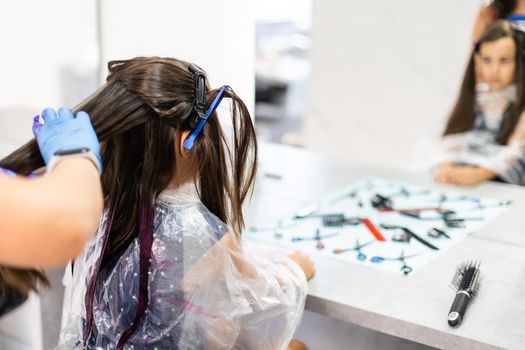 little girl dyes her hair purple in a hairdressing salon