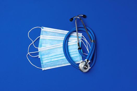 Medical face masks and stethoscope on blue background, top view