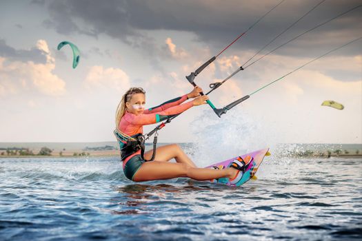 Front view Professional kite surfer woman rides on a board with a plank in her hands on a leman lake with sea water at evening. Water splashes and sun glare. Water sports.