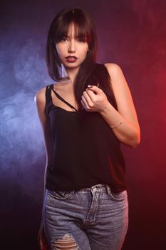 Beautiful brunette girl in shirt, jeans steps into the red and blue smoke