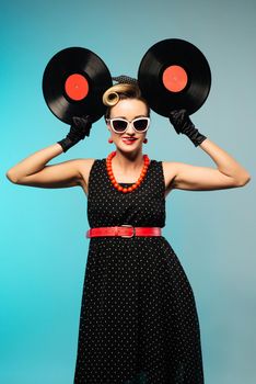 Pretty pin-up woman with retro hairstyle and make-up posing with vinyl record blue vintage background.