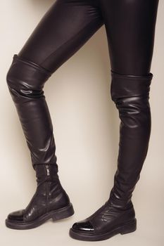 Slim women's legs in black leather pants and stylish high boots.