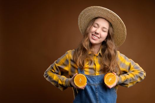 Portrait of adorable pretty playful quirky rural caucasian young woman excited cheerful casual catsuit with happy smile and closed eyes, holding cut oranges on her chest. Metaphor of healthy mammary glands and woman's health.