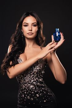 Elegant tanned woman in a beautiful dress with perfume on dark background.