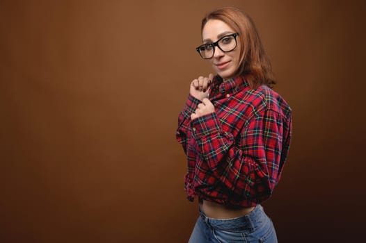 Portrait of a young attractive Caucasian woman in a red shirt and glasses on a brown background. Advertising glasses for improving vision and optics salons.