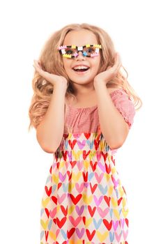 Little happy blonde girl in dress with hearts and glasses looks up side opening mouth in surprise seeing