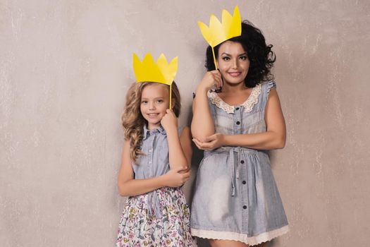 Mother and her daughter girl with a paper accessories. Mom and child are holding paper crown on stick.
