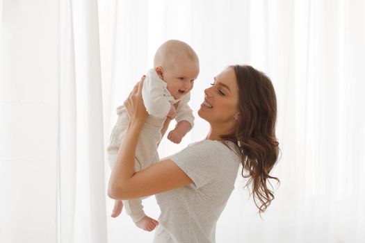 Happy smiling mother with baby having fun together on white of the curtains of the window background