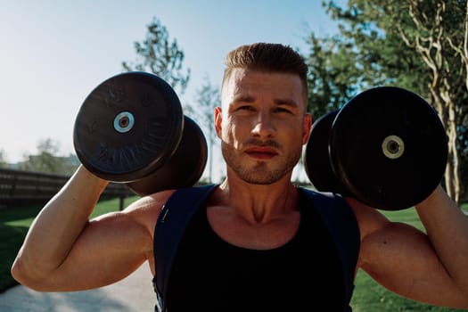 athletic man with dumbbells in his hands in the park training lifestyle. High quality photo