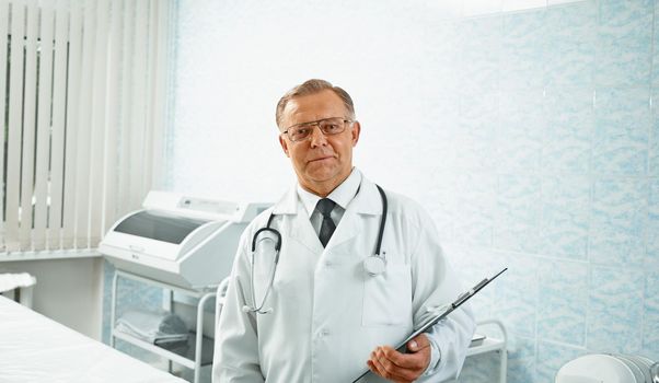 Confident senior male doctor stands with documents in hospital