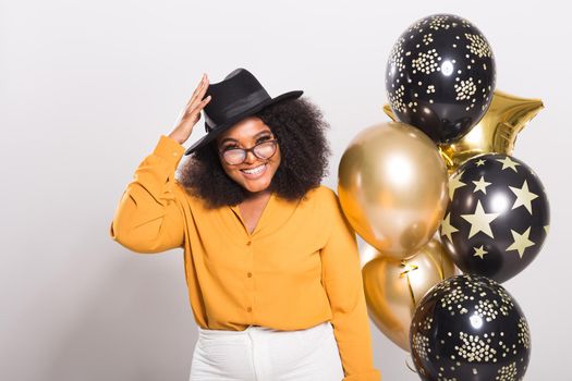 Portrait of smiling young African-American adult woman looking sweet on yellow background holding balloons.