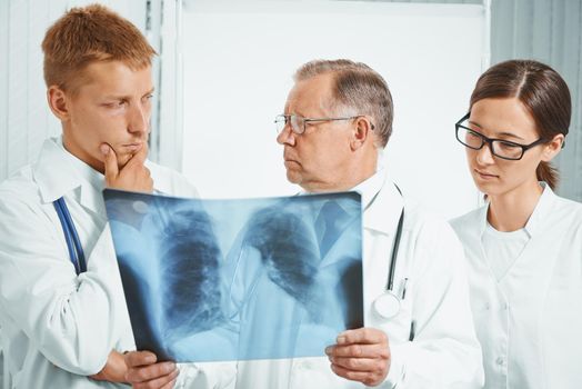 Professor older man doctor and young doctors examine x-ray image of lungs in a hospital