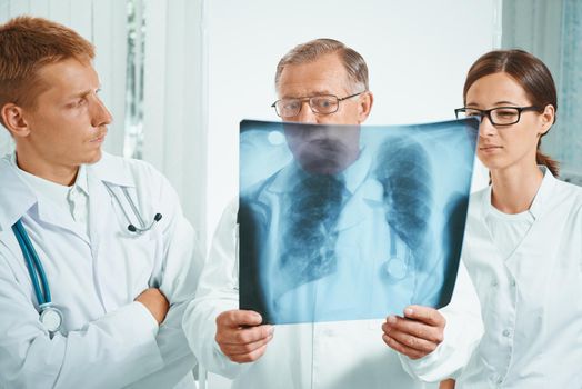 Senior man doctor and young doctors examine x-ray image of lungs in hospital