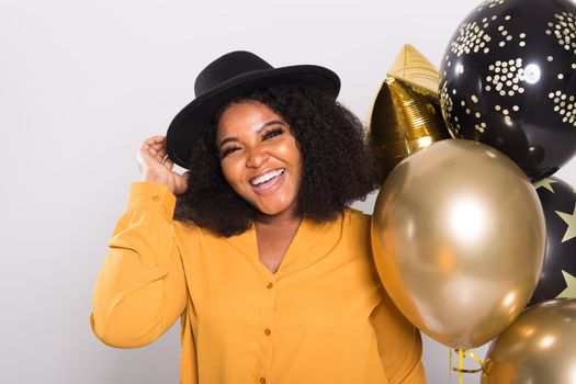 Portrait of smiling young African-American adult woman looking sweet on yellow background holding balloons.