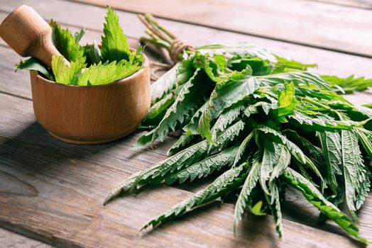 Green nettle in mortar with pestle on wooden background, medicinal herb