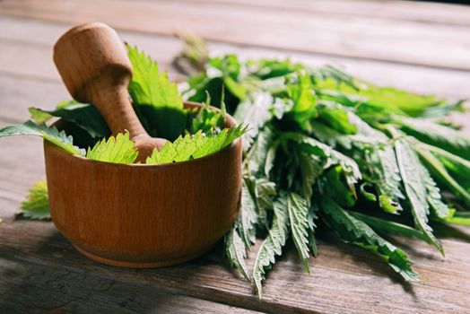 Leaves of nettle in mortar with pestle on wooden background, medicinal herb