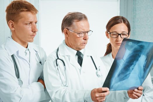 Older man doctor and young doctors examine x-ray image of lungs in hospital