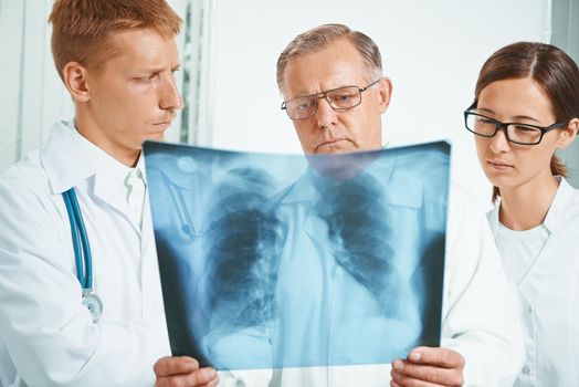 Senior man doctor and young doctors examine x-ray image of lungs in a clinic