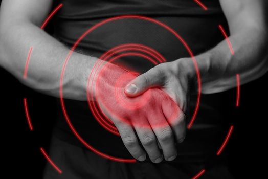 Pain in a male wrist. Man holds his hand, monochrome image, pain area of red color