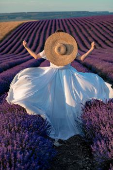 charming Young woman with a hat and white dress in a purple lavender field. LIfestyle outdoors. Back view.