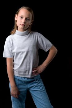 Portrait of pretty blonde preteen girl. Stylish girl dressed gray jumper posing against black background and looking seriously at camera. Close up shot of beautiful child