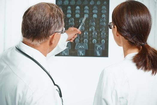 Senior doctor examines MRI image of human head. Senior man doctor teaches young woman doctor