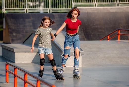 Two girls wearing roller skates riding together at park ramp. Sisters rolleblading outdoors at summer