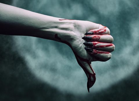 Vampire hand in blood with thumb down gesture on background of full moon. Halloween or horror theme