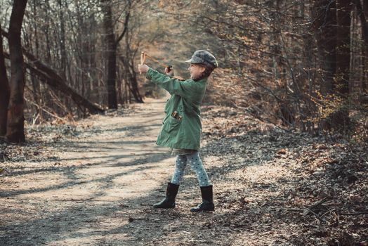 little girl playing with a slingshot in the woods, photo in vintage style