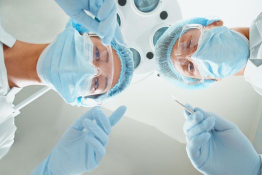 Two surgeons in protective uniform preparing for operation on background of surgical lamp