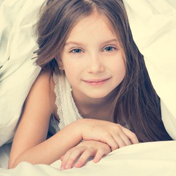 cute little girl lying in a bad under a white blanket