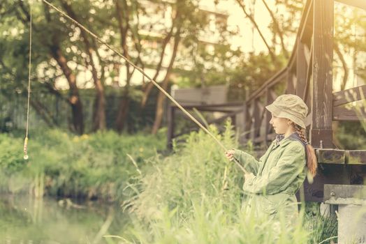 little fisher girl holdin a rod at a river near a bridge