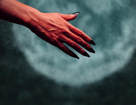 Red demon or devil hand with handshake gesture on background of full moon. Halloween or horror theme