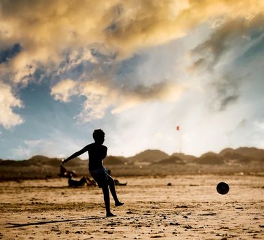 Silhouette of boy on the beach, playing football at sunset