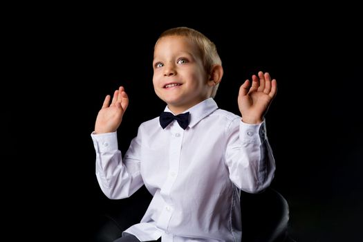 Cute little boy sitting on the armchair in the studio on a black background. The concept of family and people.