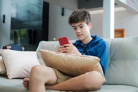The boy playing game online on smartphone at home.