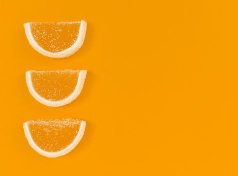 Marmalade orange slices in sugar on a orange color background with copy space.