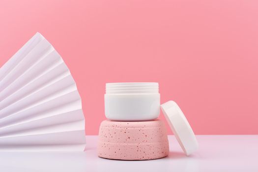 White opened cosmetic jar on pink gypsum podium against pink background with white waver and copy space. Concept of beauty product for face or hair. Face or hair cream, mask, scrub or balm