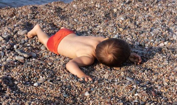 Healthy lifestyle. Little boy resting lying on the stones on the rocky beach on the Mediterranean sea