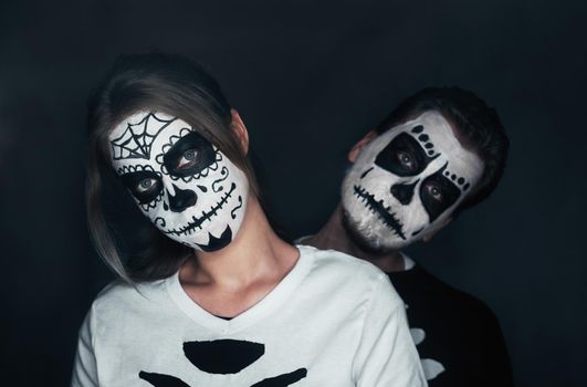 Halloween loving couple with skull face art in costume of skeletons on dark background