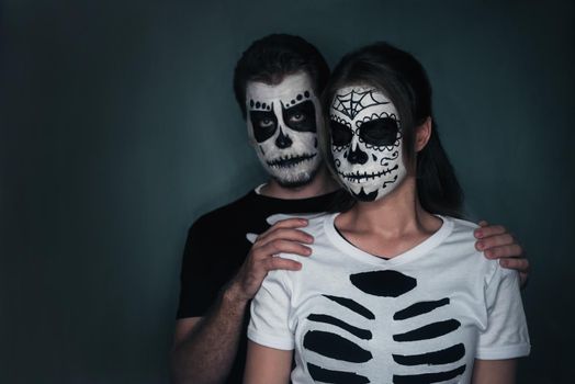 Halloween loving couple with sugar skull face art in costume of skeletons on dark background