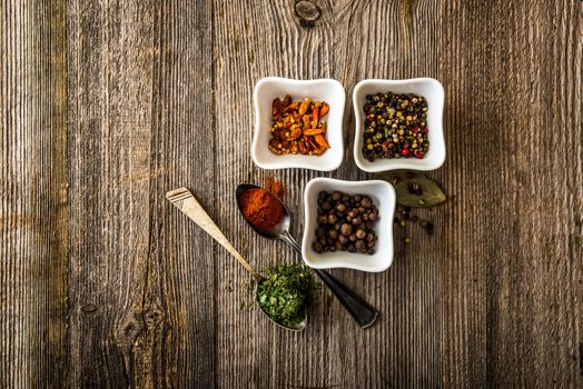 different spices in white bowls and silver spoons on wooden background
