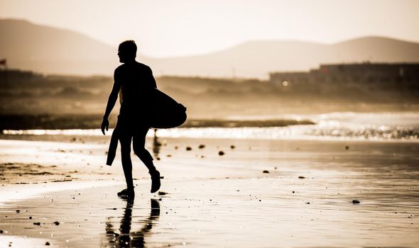Silhouette of the man walking on the beach with the surfboard
